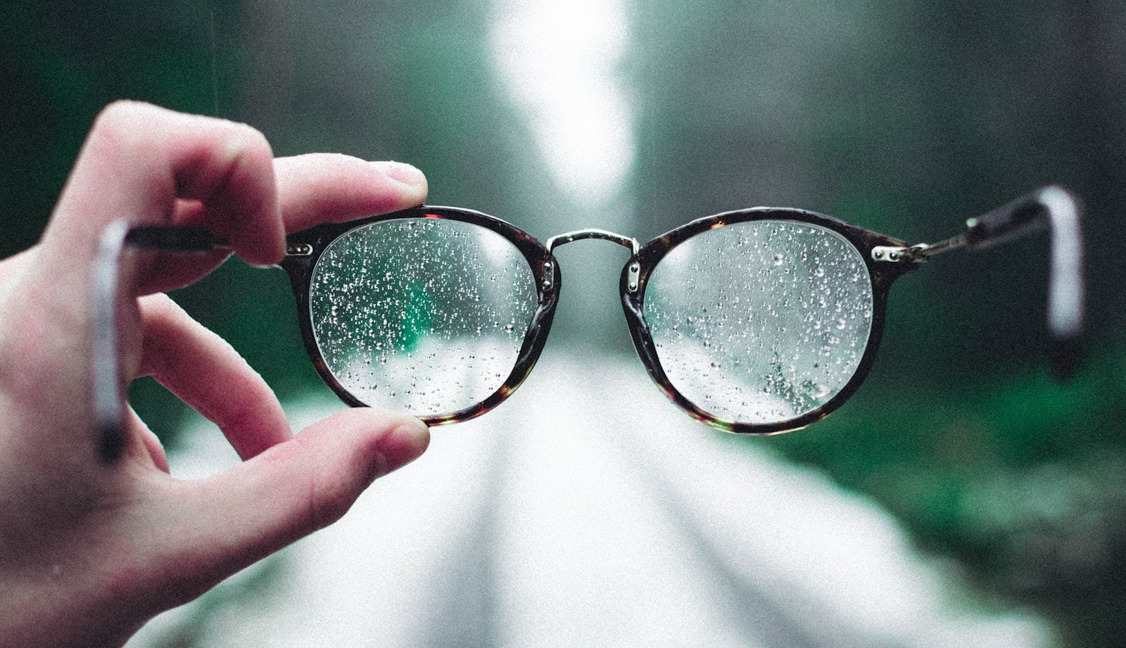 Hand holding eyeglasses covered in water droplets on a fogged grey background