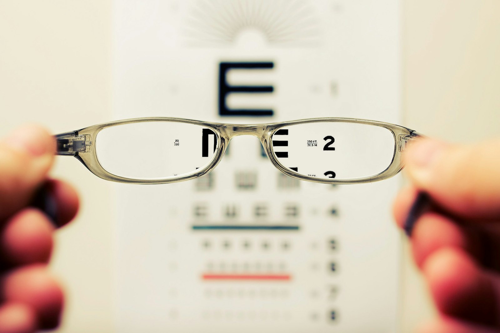 Hands holding eyeglasses up toward an eye chart, with the letters sharp and clear through the lenses