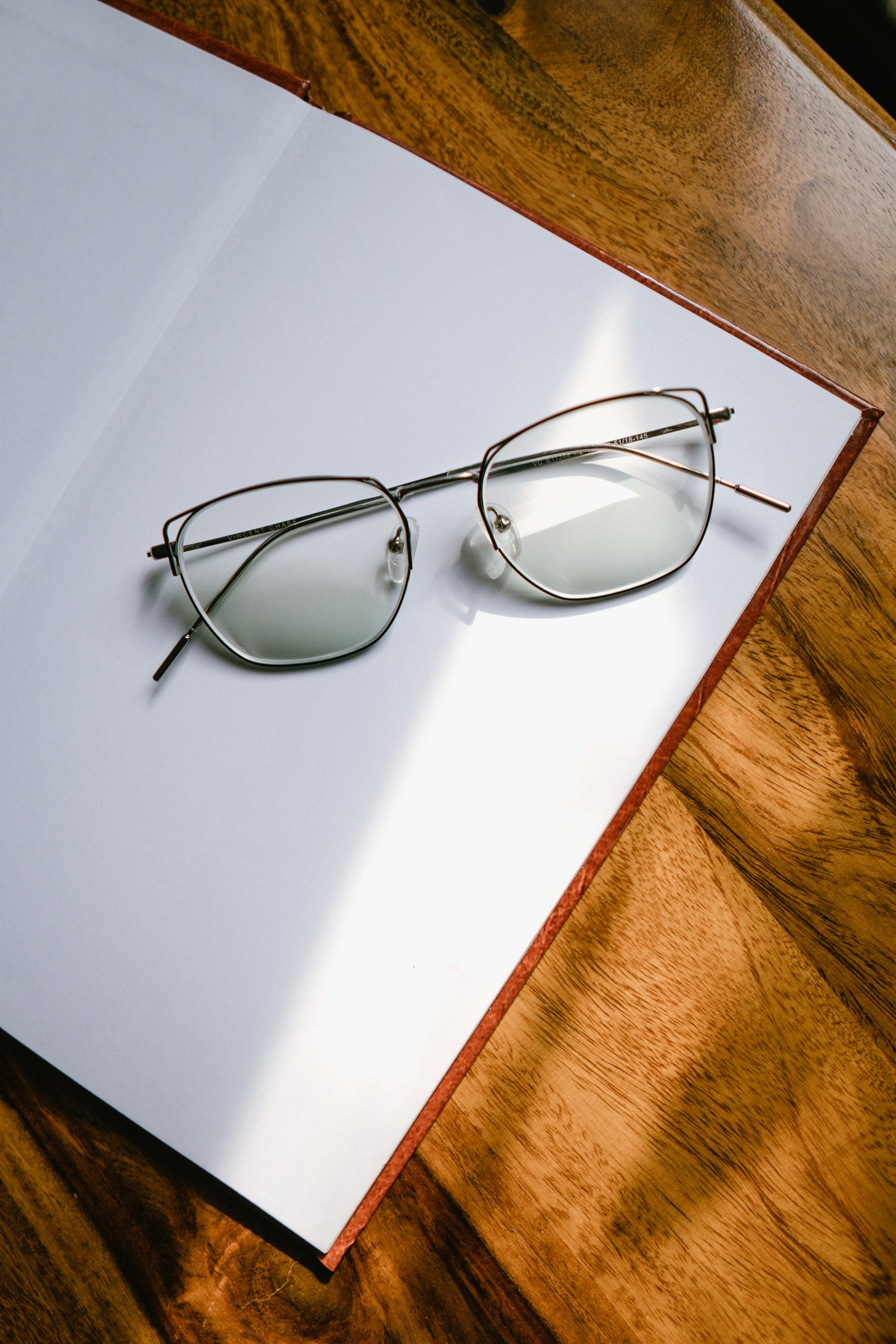 Black framed eyeglasses on a clean surface, lenses visible with light reflection