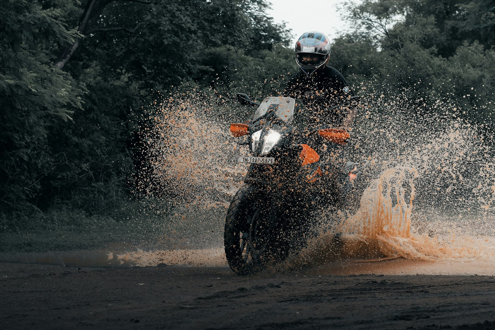 Motorcycle rider in a full-face helmet riding through standing water in wet conditions