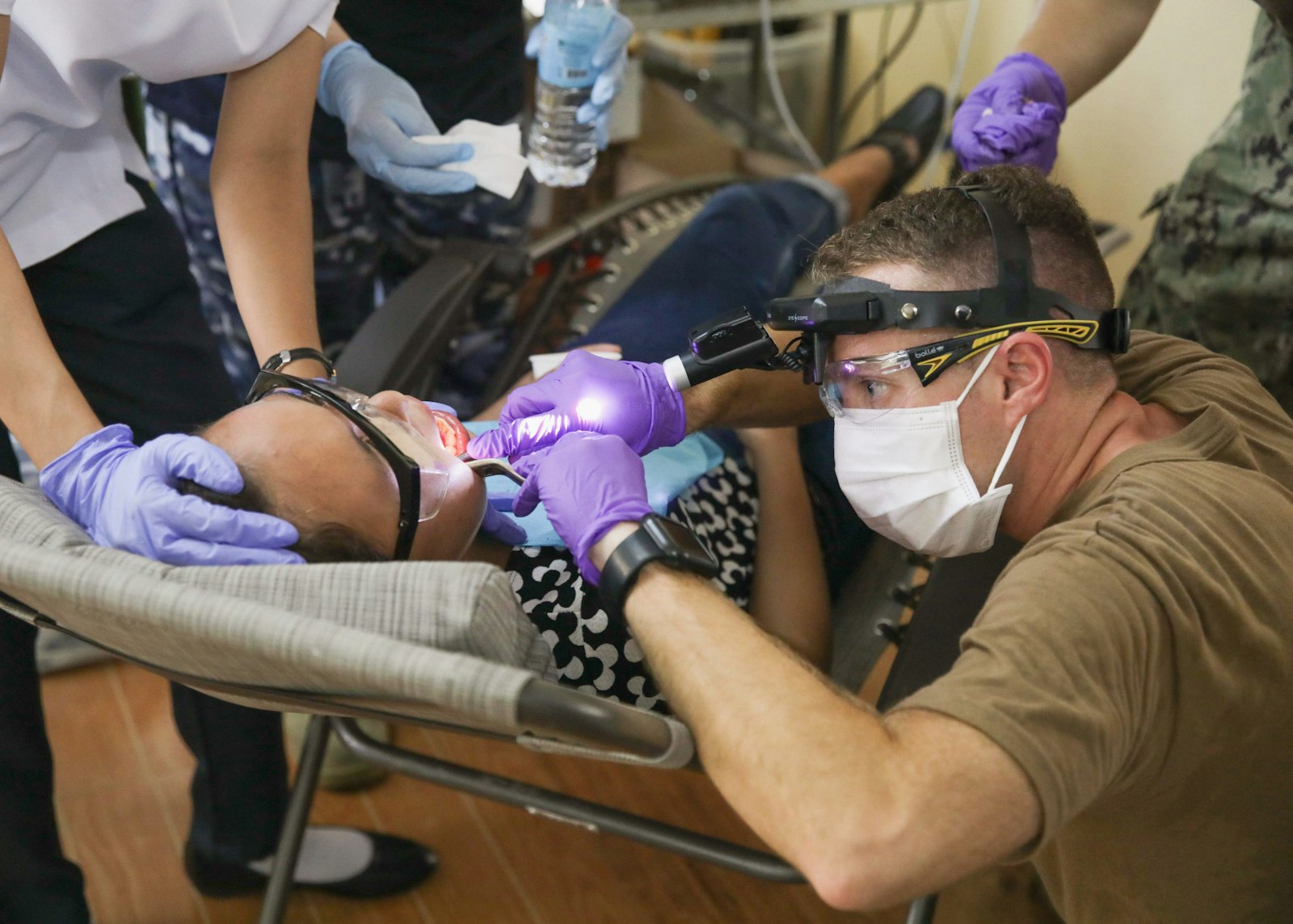 Dentist performing procedure on a patient with assistance in a clinical setting